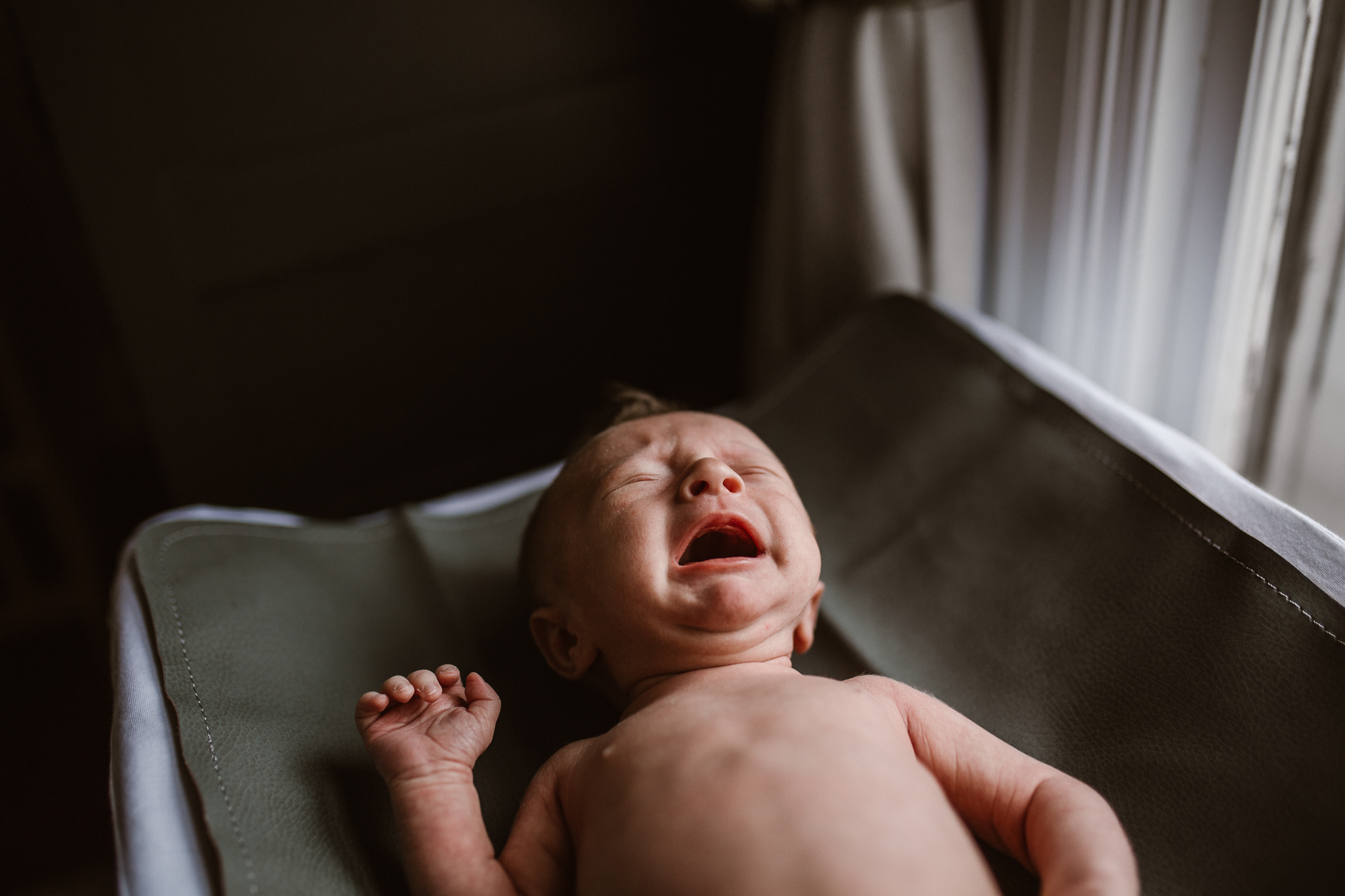 Newborn baby crying on the changing pad next to the window.
